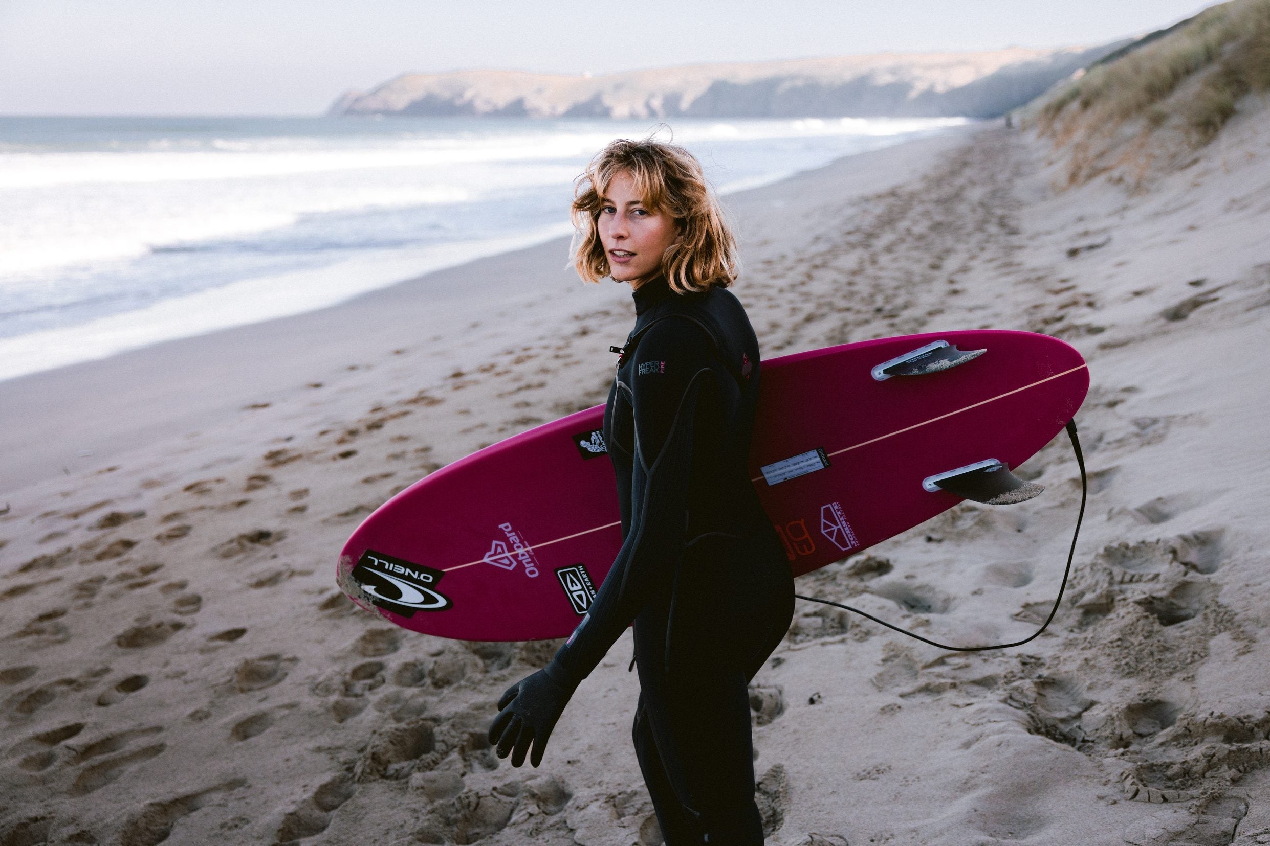 Woman ready to brave the cold in a premium 5+mm winter wetsuit, selected by the experts at Noordzee Boardstore. Noordzee Boardstore surfshop Surfschool webshop surfboardrepairs Scheveningen