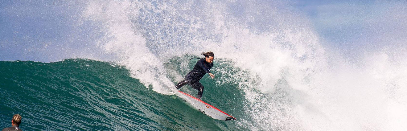 Advanced surfer holding a high-performance shortboard, showing the quality gear available at Noordzee Boardstore. Noordzee Boardstore surfshop Surfschool webshop surfboardrepairs Scheveningen