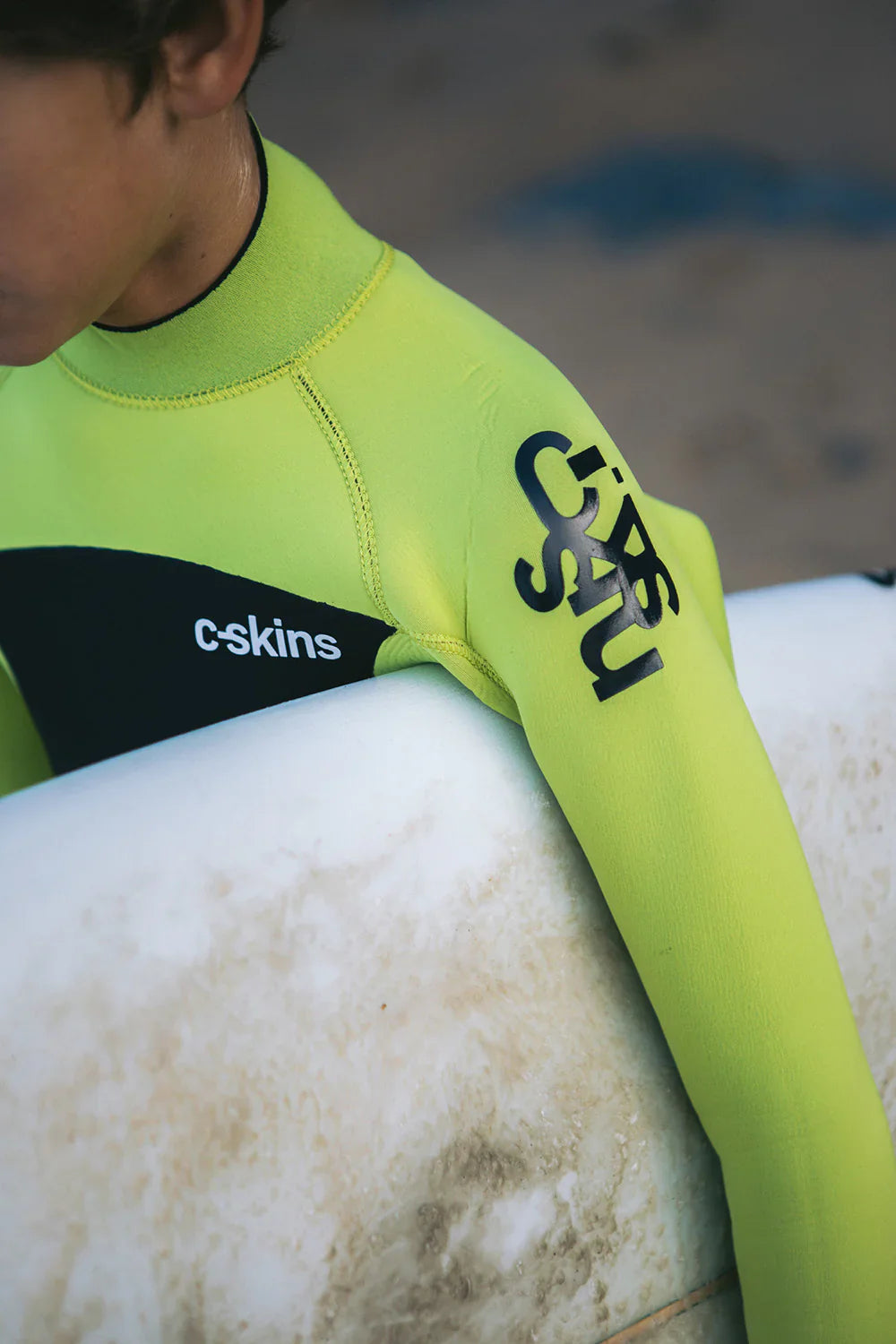 A happy young surfer holding their new junior wetsuit from Noordzee Boardstore. Noordzee Boardstore surfshop Surfschool webshop surfboardrepairs Scheveningen