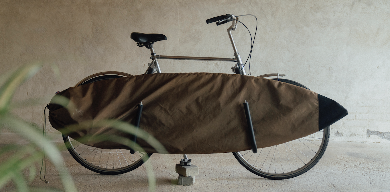 A person cycling to the beach in Scheveningen with their board securely on a bike rack from our shop. Noordzee Boardstore surfshop Surfschool webshop surfboardrepairs Scheveningen